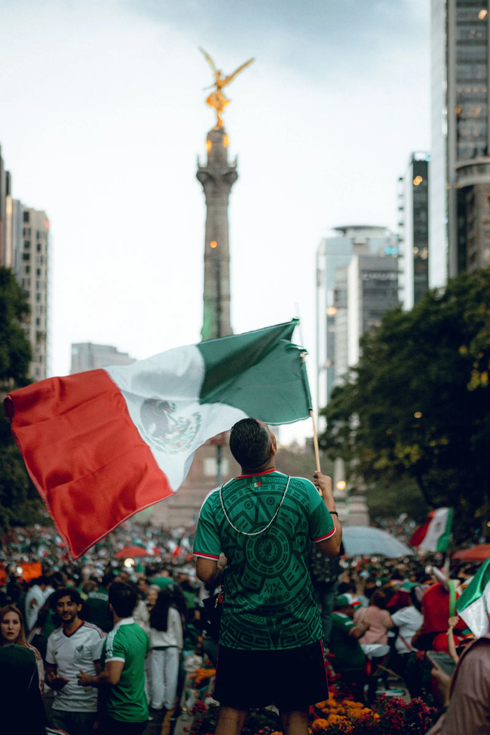 Mexico Joins Global Rules Wave Reshaping Platforms for Minors A crowd celebrates at the Angel of Independence in Mexico City beside a large Mexican flag.